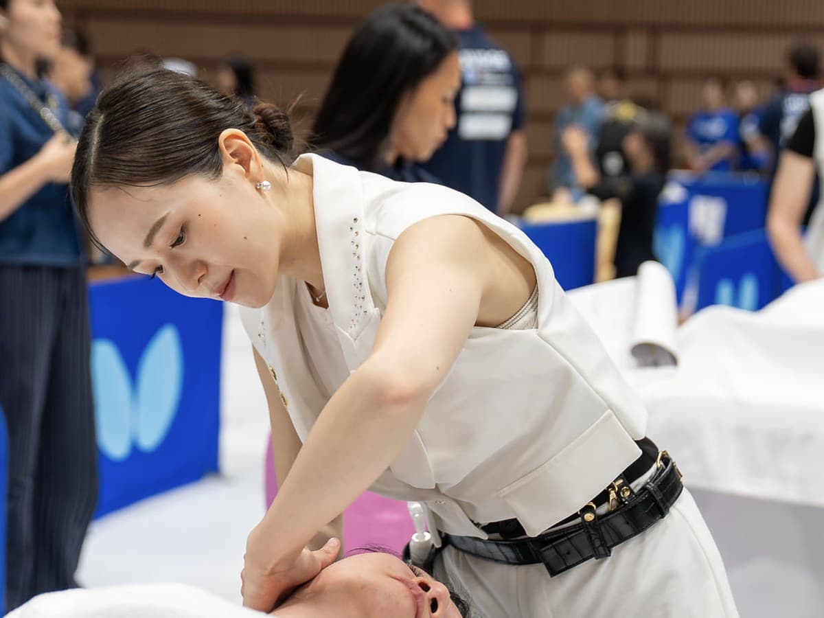 في فئة Facial ضمن AMC2026، امرأة ترتدي الأبيض تعتني بوجه متلقية مستلقية على ظهرها