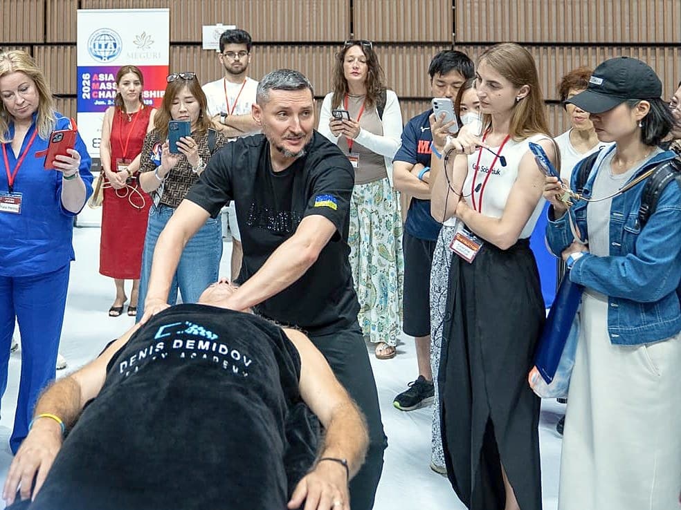 Tại workshop của AMC2026, giảng viên của một học viện làm đẹp trình diễn kỹ thuật trên người nhận nằm ngửa, các học viên xung quanh quay bằng điện thoại